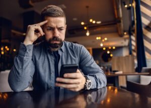 Concerned man looking at his phone in a modern café, representing cautious consumer behavior in a slow economy